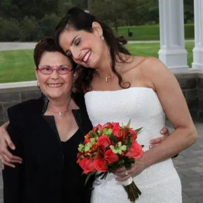 Estelle Vernon with a smiling bride holding a bouquet on her wedding day, both wearing elegant jewelry.